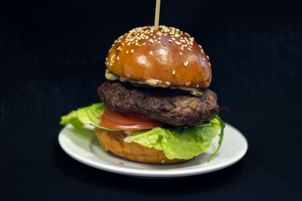 Burger z dzika na białym talerzu z wbitą w niego wykałaczką