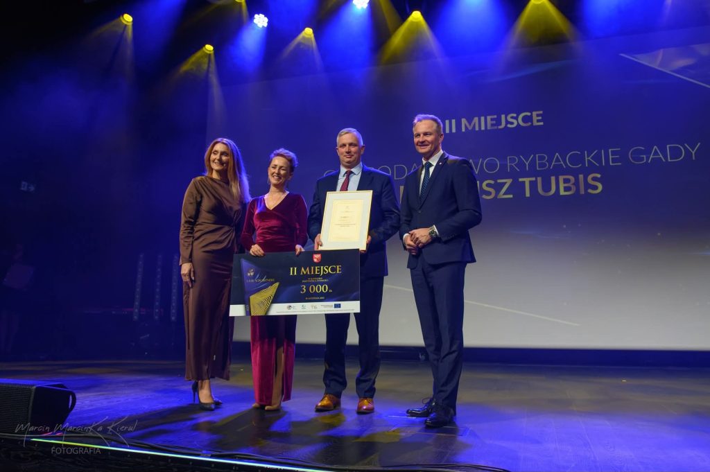 Marlena i Dariusz Tubis stojący z nagrodami na scenie wraz z Marszałkiem Marcinem Kuchcińskim oraz Wicemarszałkini Sylwią Jaskulską