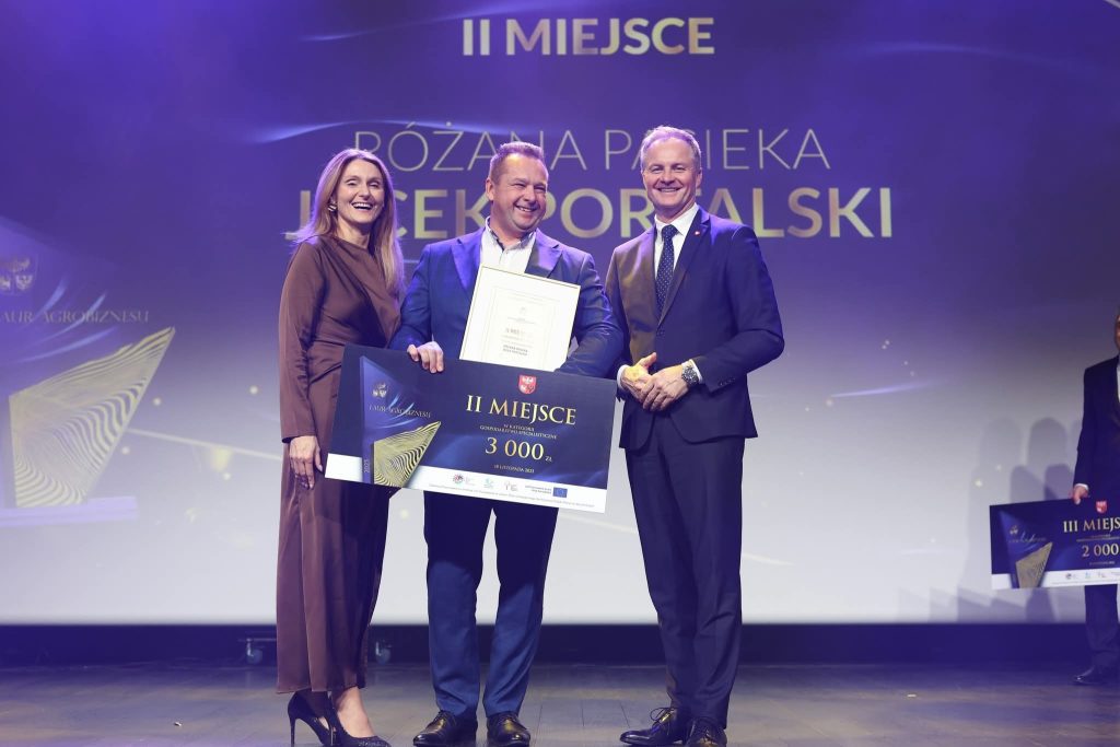 Jacek Portalski stojący z nagrodami na scenie wraz z Marszałkiem Marcinem Kuchcińskim oraz Wicemarszałkini Sylwią Jaskulską