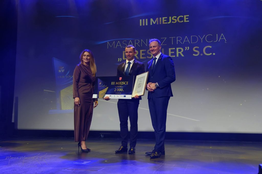 Bartosz Dreszler stojący z nagrodami na scenie wraz z Marszałkiem Marcinem Kuchcińskim oraz Wicemarszałkini Sylwią Jaskulską